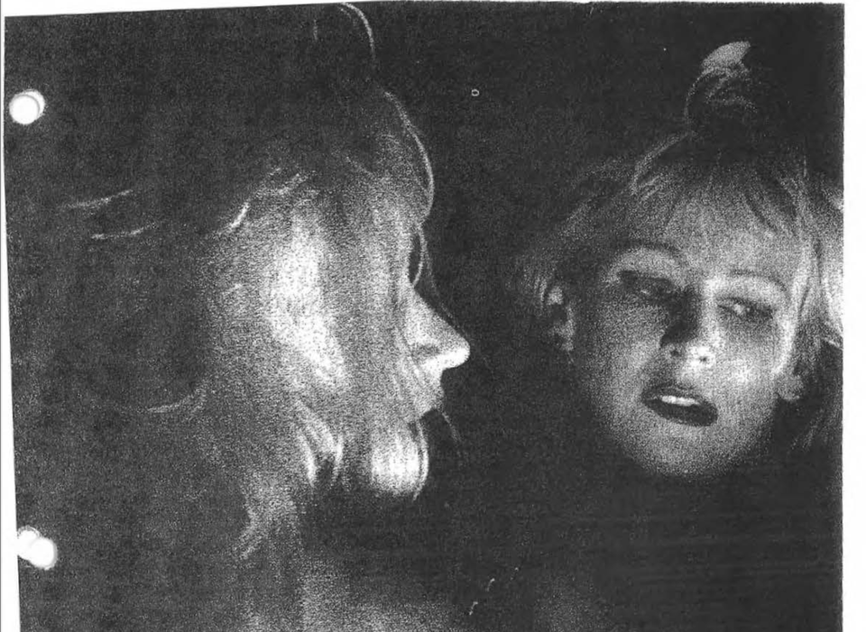 Grainy black and white image of a blonde woman in heavy makeup looking in a mirror, her expression remote and dissociated