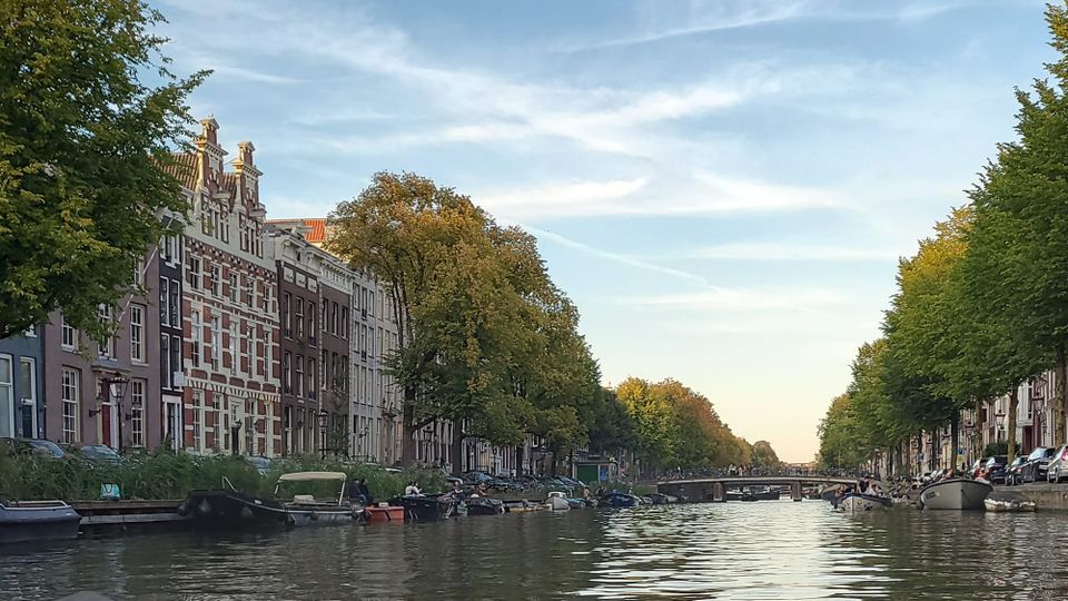 Tree-lined canals near the Internet Archive Europe HQ. Tall 17th/18th-c. buildings; wispy clouds in a light-filled sky; rippling water, a low bridge visible in the distance.