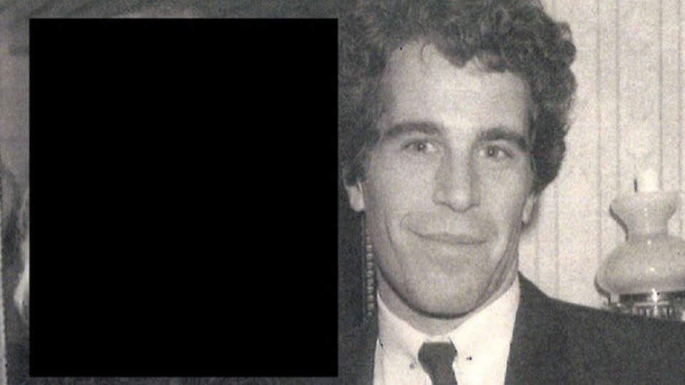 Black and white photograph of Jeffrey Epstein and a redacted-face companion; he's wearing a dark suit and tie, white shirt and a tie bar
