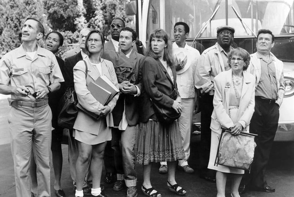 A black and white still from 'Jury Duty' with eleven actors, character-actorishly dressed, all looking u quizzically in the same direction
