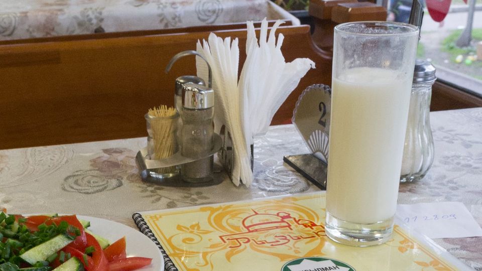 Detail photo of a halal restaurant lunch in Almaty, Kazakhstan, showing colorful menu, a salad, and a tall glass of kumis.