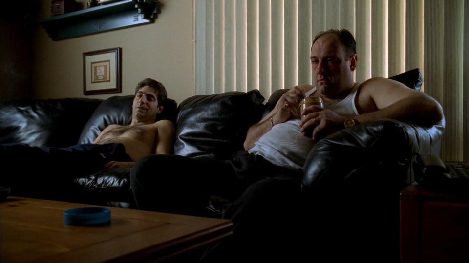 Shirtless Christafuh and A-shirt Tony sitting on a black leather couch probably sticking to it. Tony is eating peanut butter out of a jar with a spoon.