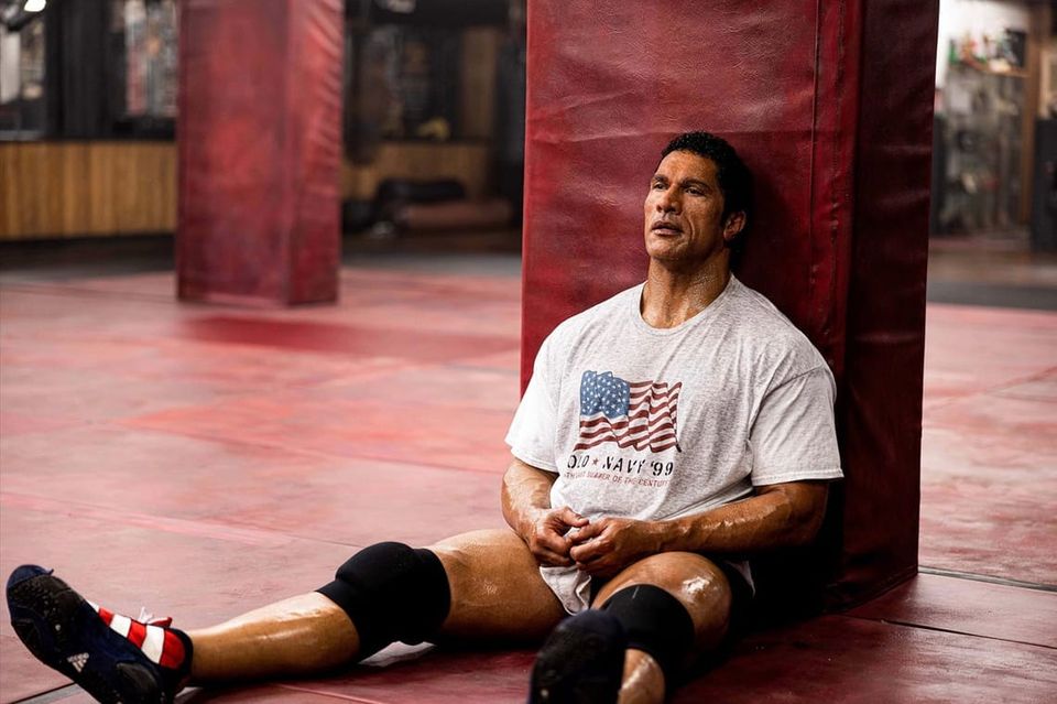 Johnson as mixed-martial arts and UFC champion, Mark Kerr, looking exhausted and sweaty, sitting on the floor in a training room lined with red padding
