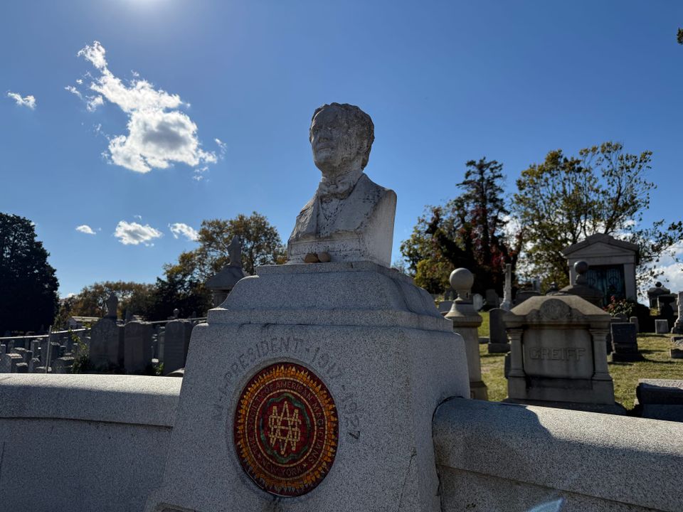 The tomb of Harry Houdini, with sculpted stone bust, rich blue sky and trees in the background