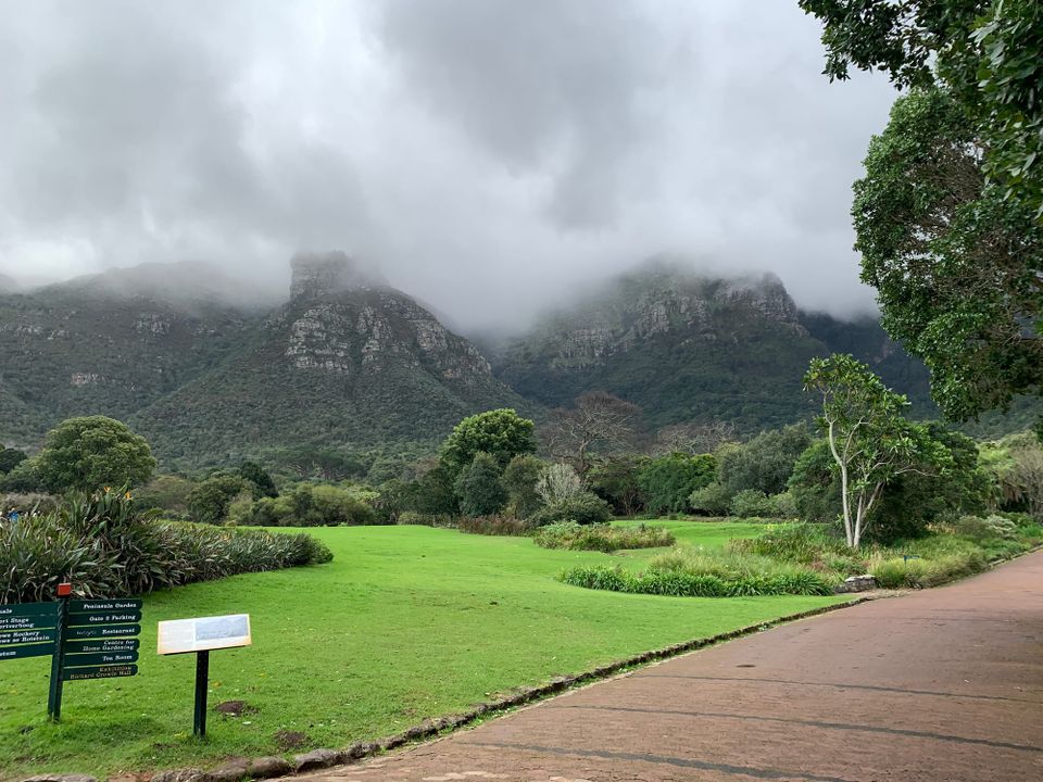Rocky hills topped with glistening mists; a verdant garden below, with signs to guide visitors in the foreground