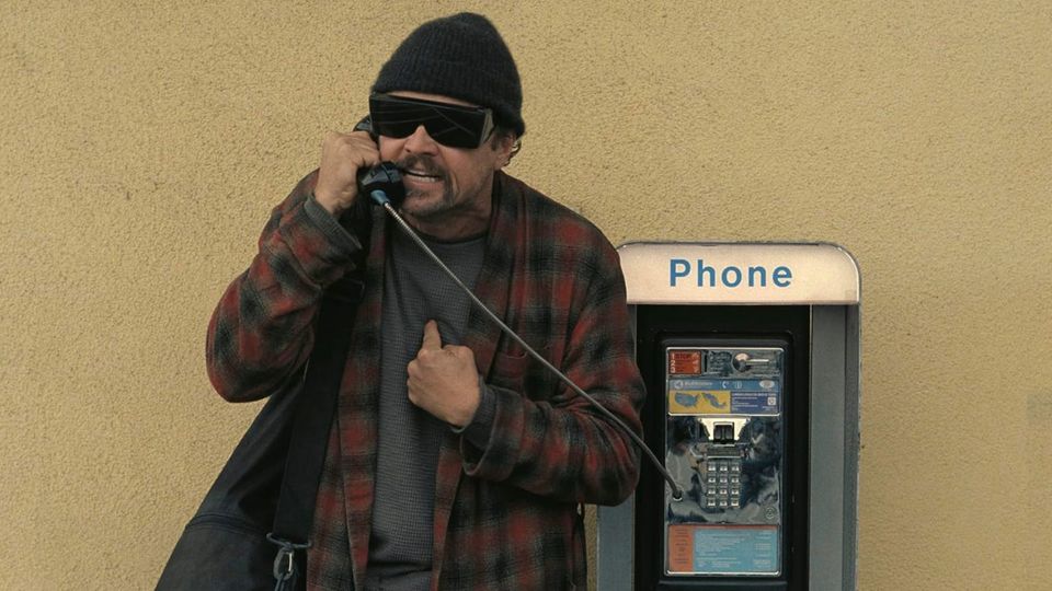 An angry Leonardo DiCaprio in big dark glasses and a Pendleton, nostrils flared, snarling into the handset of a 1980s pay phone