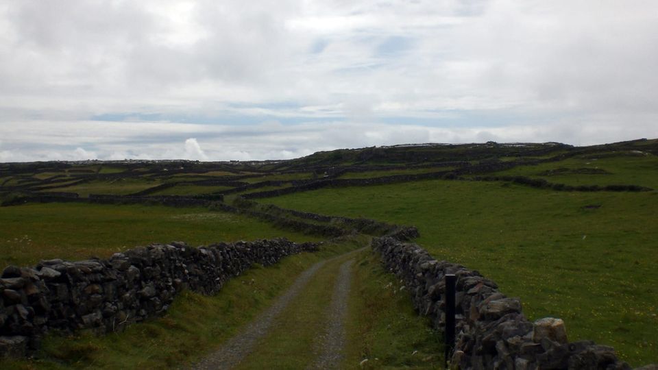 A spooky stone-walled path on the island of Inis Mór runs through emerald-green fields under a darkening, cloudy sky