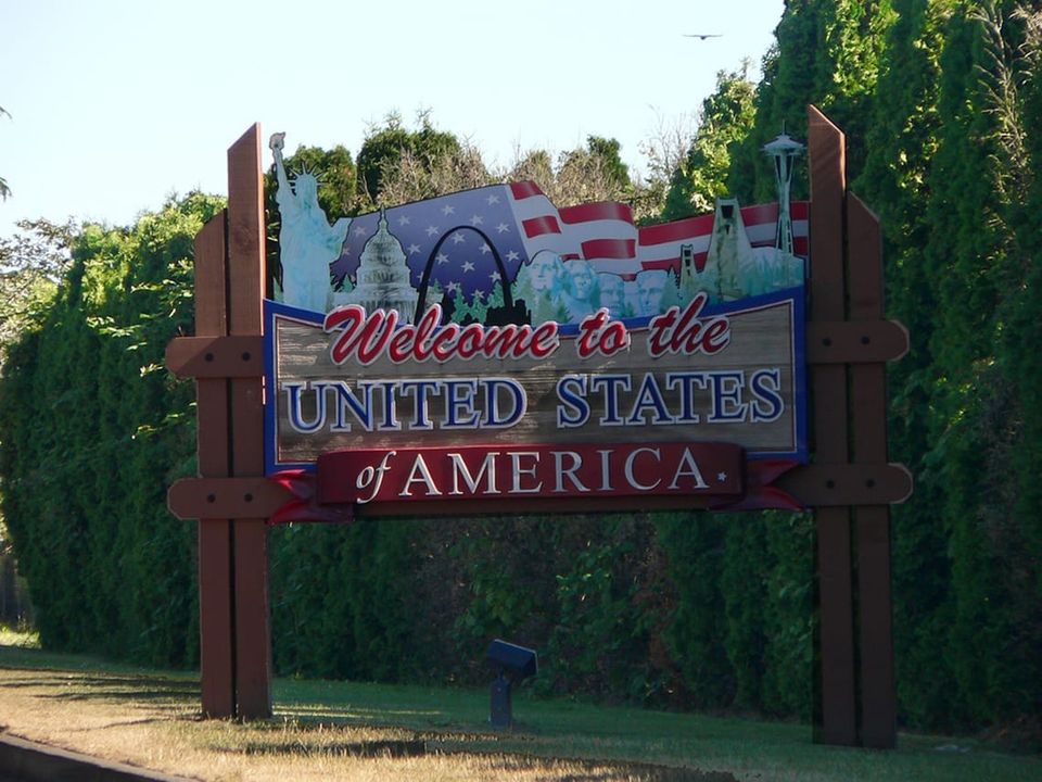 Colorful wooden sign WELCOME TO THE UNITED STATES OF AMERICA featuring Statue of Liberty, US Capitol dome, Mount Rushmore, Golden Gate Bridge, and Space Needle.