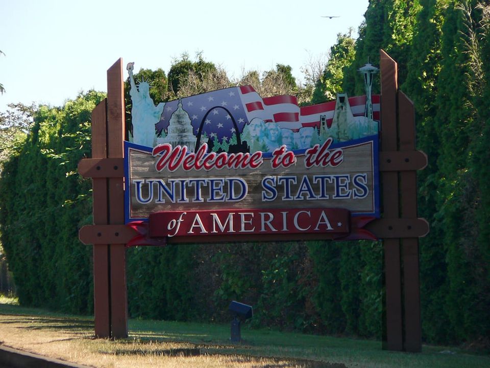 Colorful wooden sign WELCOME TO THE UNITED STATES OF AMERICA featuring Statue of Liberty, US Capitol dome, Mount Rushmore, Golden Gate Bridge, and Space Needle.