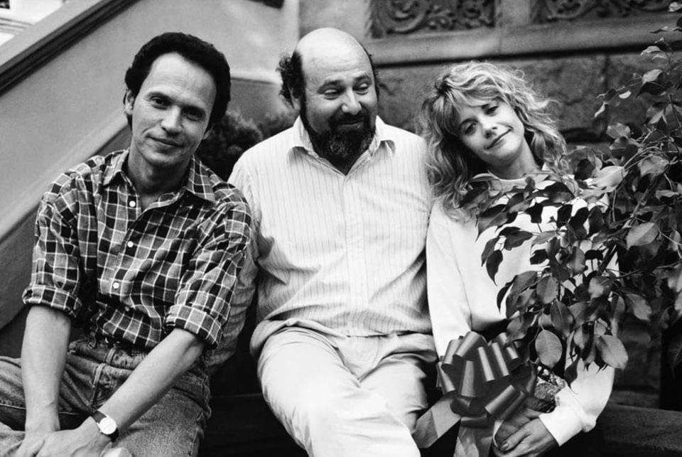 A b&w publicity shot of Rob between Billy and Meg, who is holding a potted plant with a ribbon on it.