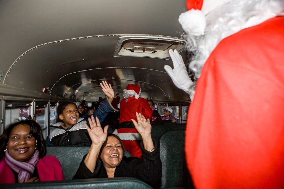 Santas walking through a bus being greeted with smiles and cheers from young and old alike