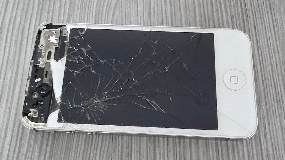 A badly smashed iPhone lying on a flat woodgrained surface