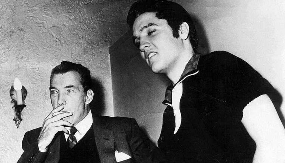 Black and white image of Ed Sullivan and Elvis Presley in 1956; Sullivan is smoking a cigarette, Presley in a short sleeved polo