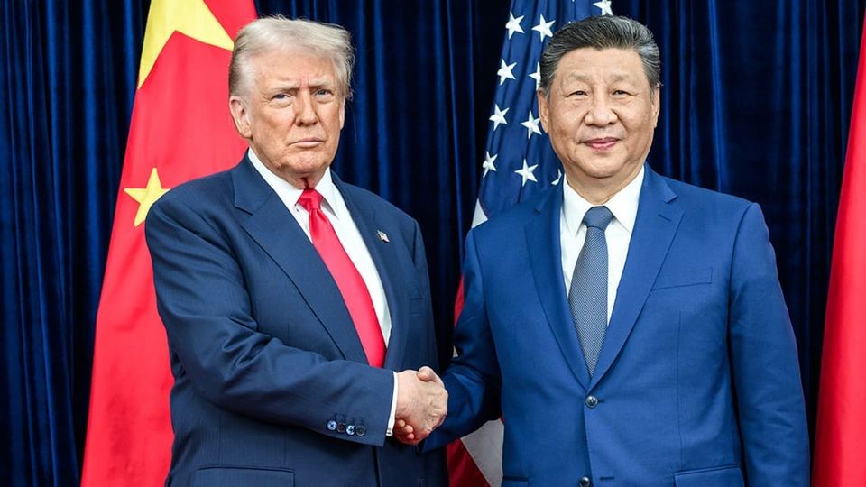 The two men stand before US and China flags shaking hands while looking into the camera for the photo-op