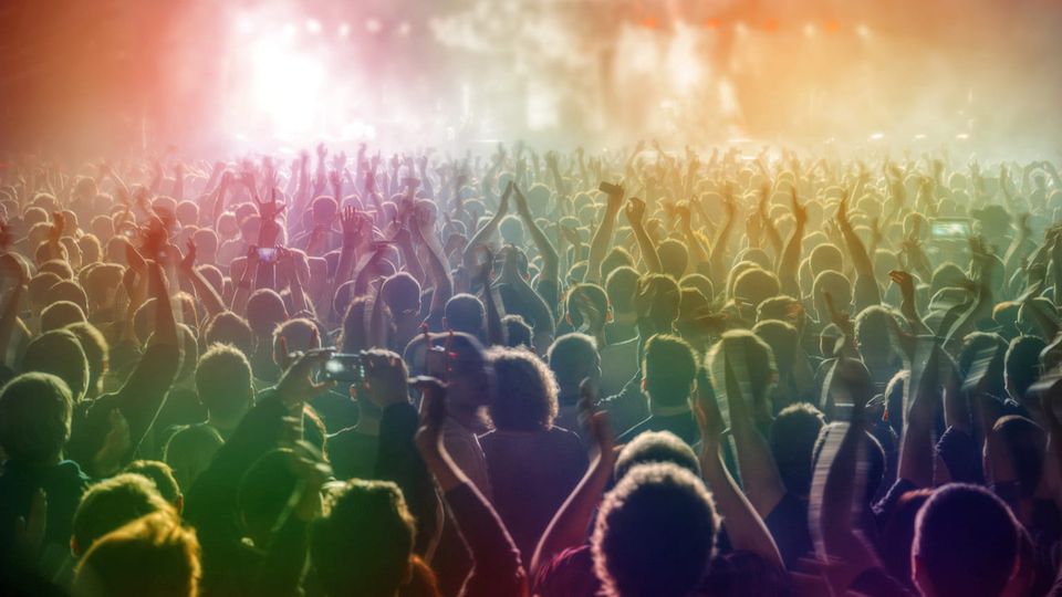 Crowd at a show viewed from behind hazy atmosphere, golden lights onstage, everyone almost silhouettes