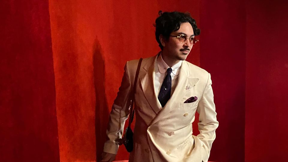 Handsomely dressed dark-haired author in a double-breasted cream suit with a paler shirt, dark tie, shirt with collar bar, and brown pocket square
