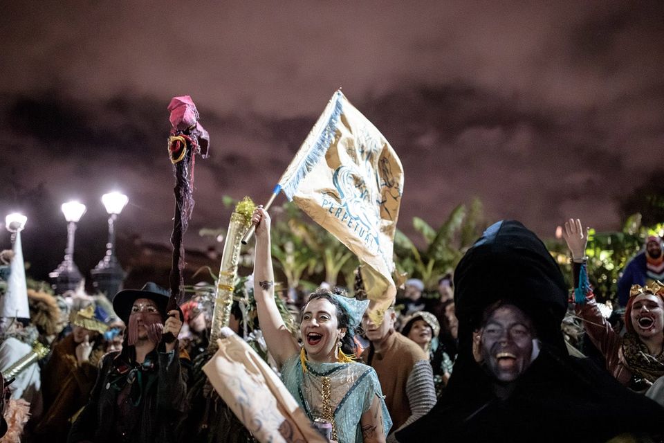Smiling revelers dressed in wild festive costumes, one with a festival flag held aloft