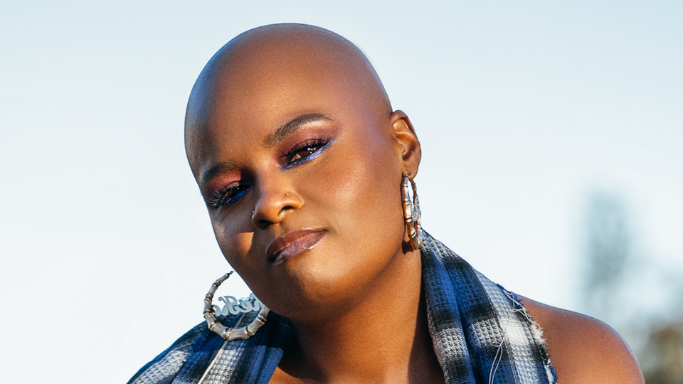 Portrait of Keeonna Harris, a Black woman wearing blue eyeliner and bamboo earrings, in blue and grey plaid