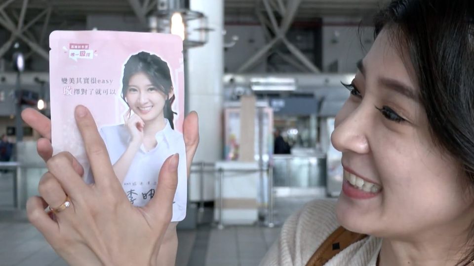 Smiling Taiwanese woman holding up a promotional packet printed with her likeness and campaign message)