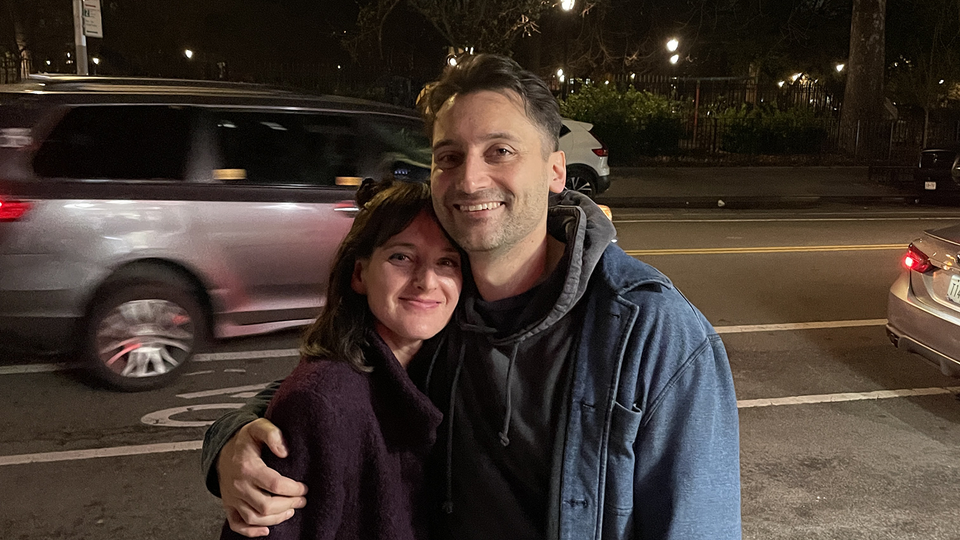 Ben Collins and Lindsey Adler, at night on a city sidewalk with cars speeding past behind them