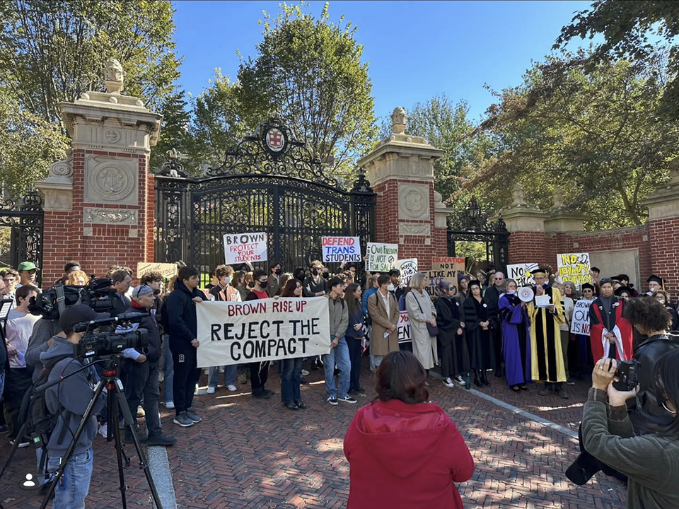 Student demo before the gates of Brown University, October 2025, with signs: BROWN RISE UP REJECT THE COMPACT; BROWN PROTECT YOUR STUDENTS; DEFEND TRANS STUDENTS