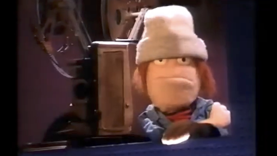 Puppet projectionist wearing a soft hat and slightly truculent expression