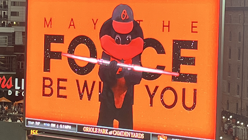 On the big screen at stadium: Orioles bird mascot brandishing a double-dong lightsabre in front of graphic: MAY THE FORCE BE WITH YOU