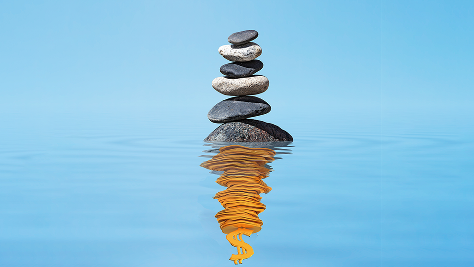 Zen stones balanced in a stack in a rippling pool and the reflection is gold coins in a stack topped with a dollar sig