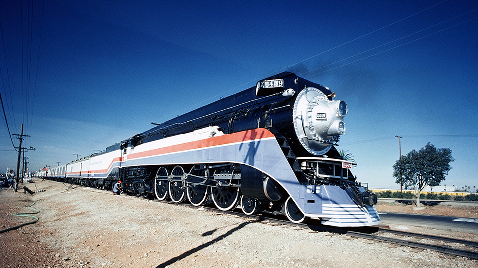 Red, white, and blue No. 4449 on tracks with wisp of black smoke in deep clear blue sky.