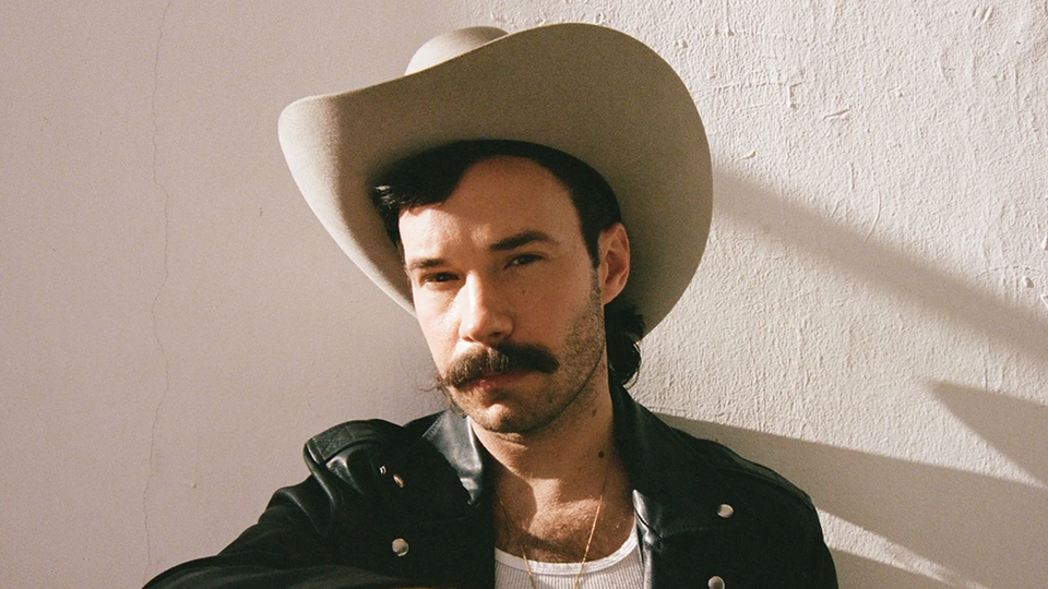 A mustachioed gentleman in a leather jacket and a buff cowboy hat