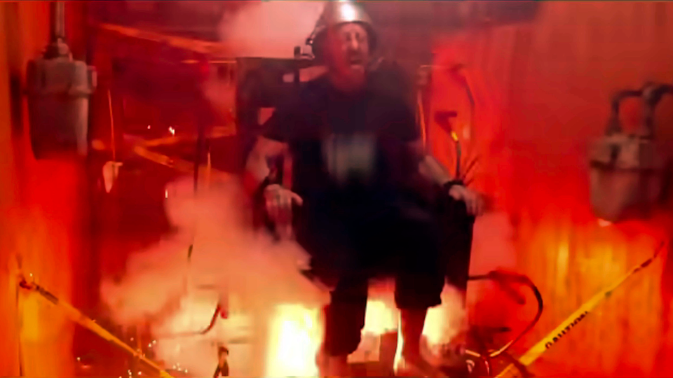 A man seated in what appears to be a violently discharging electric chair screaming in pain.