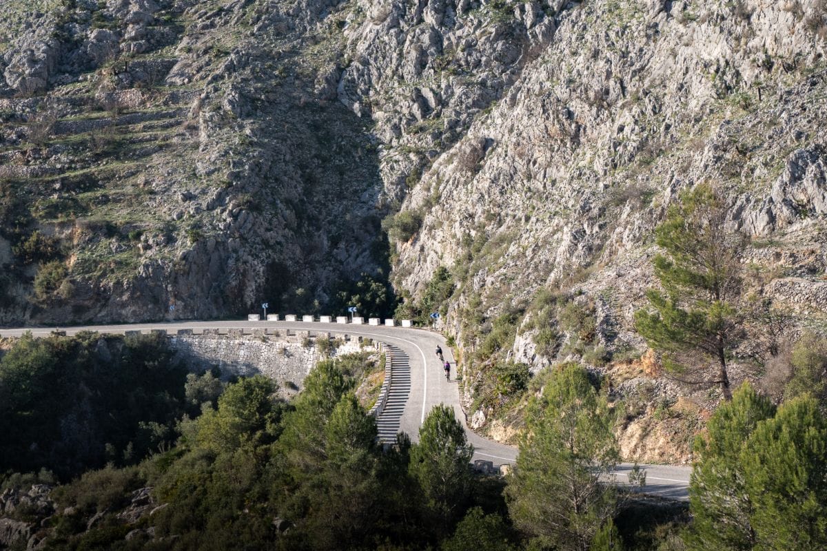 Two cyclists descending the winding mountain roads of Vall de Ebo with a scenic mountain landscape.