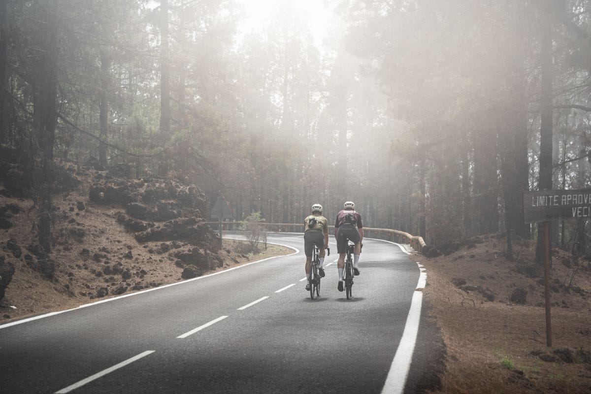 Two cyclists on a smooth road riding up Mount Teide, with dramatic mist and volcanic landscapes in the background, showcasing the epic microclimate and nature of Europe’s longest climb.