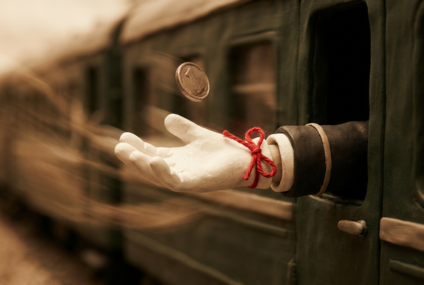 A gloved hand reaches from a train window, palm open, as a coin falls toward it, a red thread tied at the wrist.