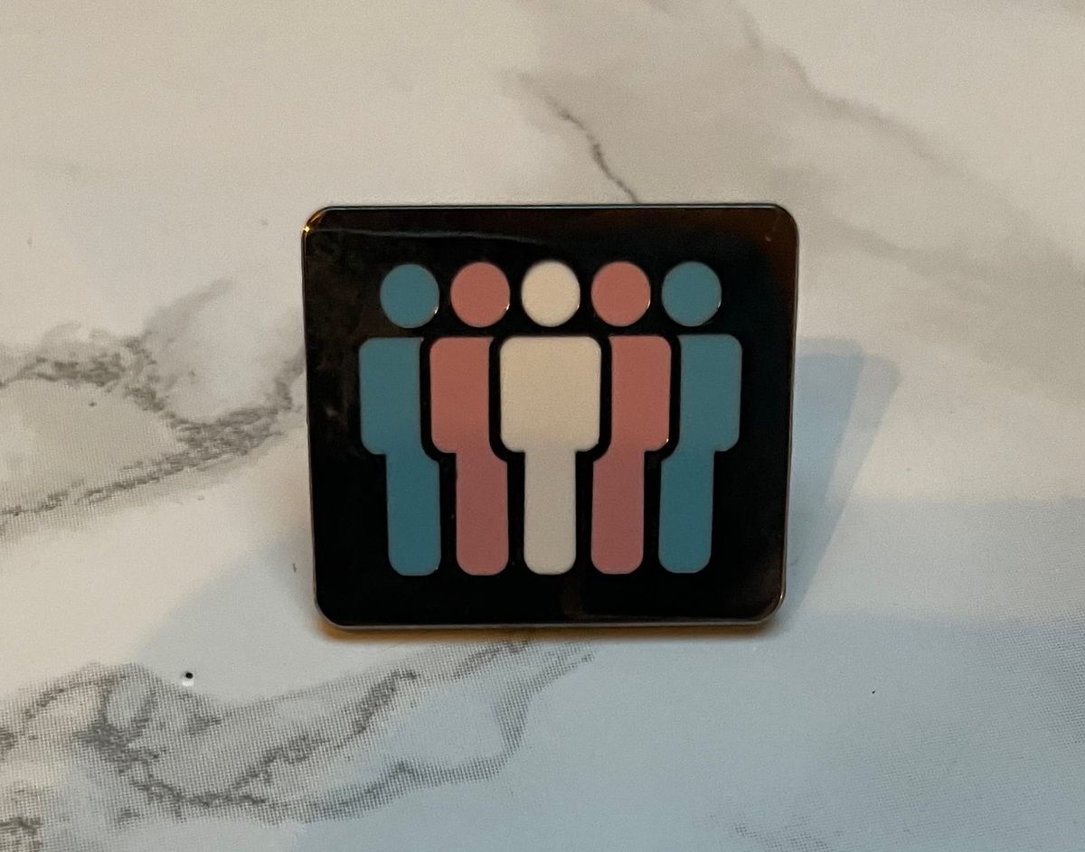 A pin from Trans and Gender Queer Houston (TGQH), sitting on a faux-marble desk.  