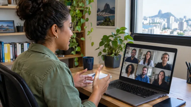 Profissional brasileiro conduzindo uma reunião por vídeo em casa com a equipe em tela (imagem ilustrativa gerada por IA)