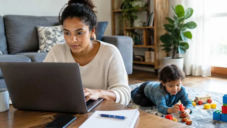 Ilustração gerada por IA: mãe trabalhando no notebook com criança brincando ao lado.