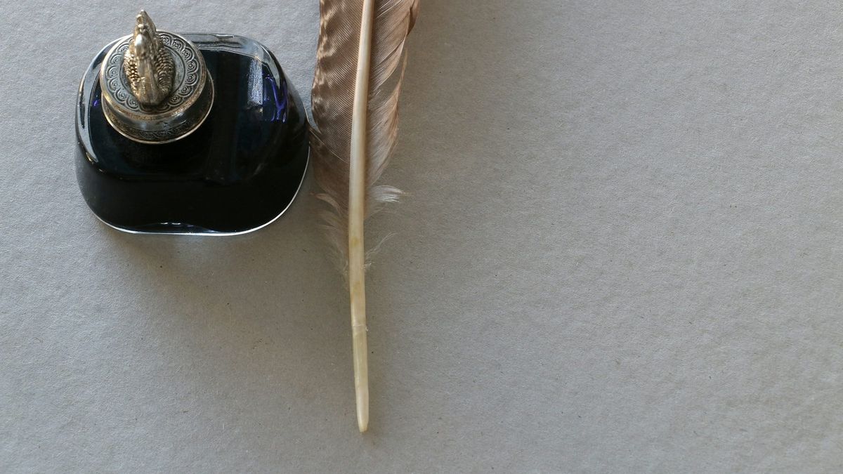 Closeup of an antique ink bottle and quill pen on a sheet of paper.