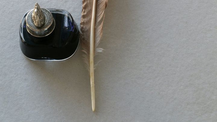 Closeup of an antique ink bottle and quill pen on a sheet of paper.