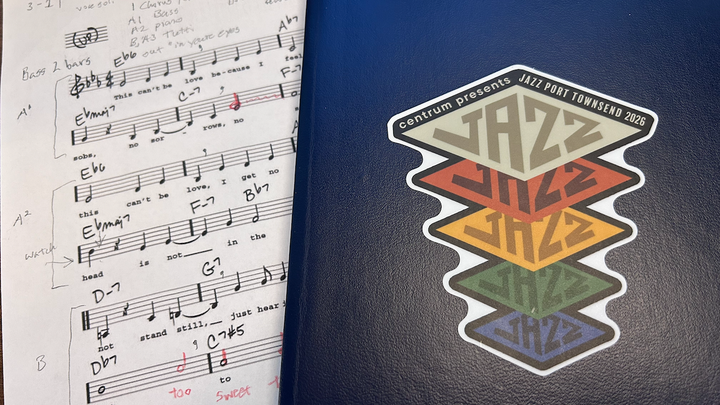 A marked up sheet of music half covered by a notebook with a Jazz Port Townsend 2026 sticker on it.