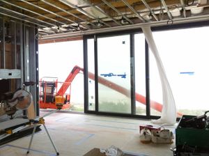 A residential construction job site with exposed studs in the walls and ceilings, and glass sliding doors open to a crane.