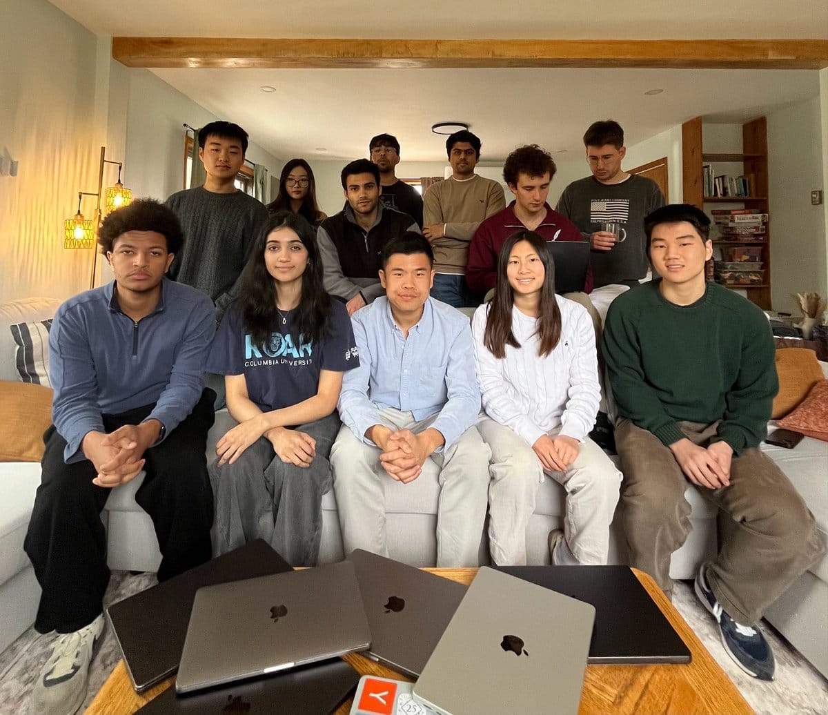 students sat around a table full of macbooks, ready to do a hackathon