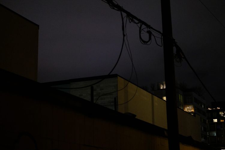 A picture of the night sky between rooftops glowing purple-grey; Mount Pleasant, Vancouver