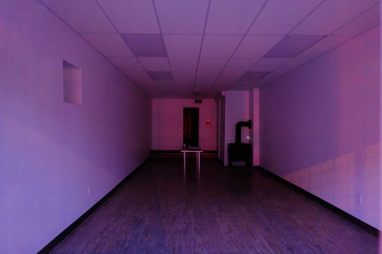 An empty retail space but for a single white table and furnace bathed in magenta light; Victoria-Fraserview, Vancouver