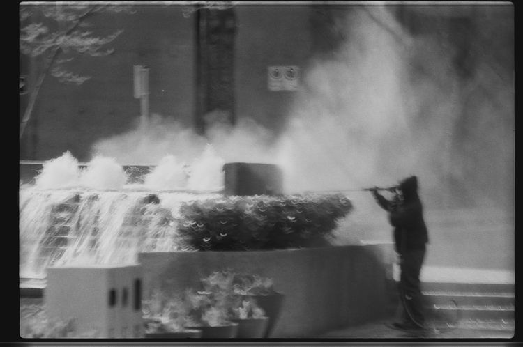 Worker washes a fountain with a pressure washer, taken from a moving bus