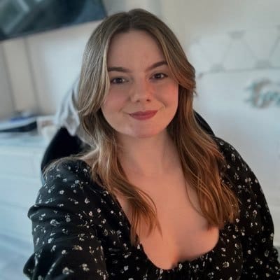 @C9EmZ on Twitter looking happily at the camera wearing a black floral shirt against a light colored background