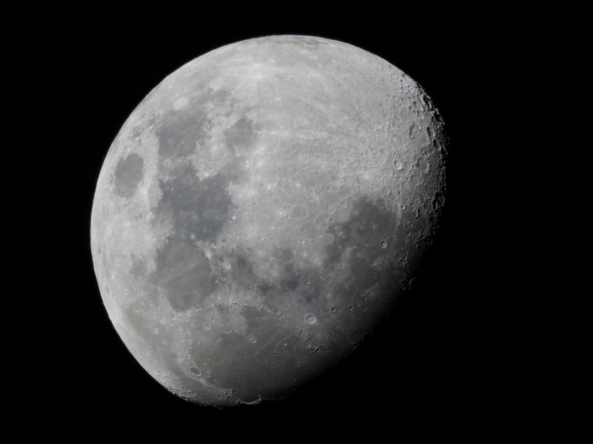 A black and white image of the moon, three-quarters illuminated. 