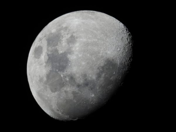 A black and white image of the moon, three-quarters illuminated. 