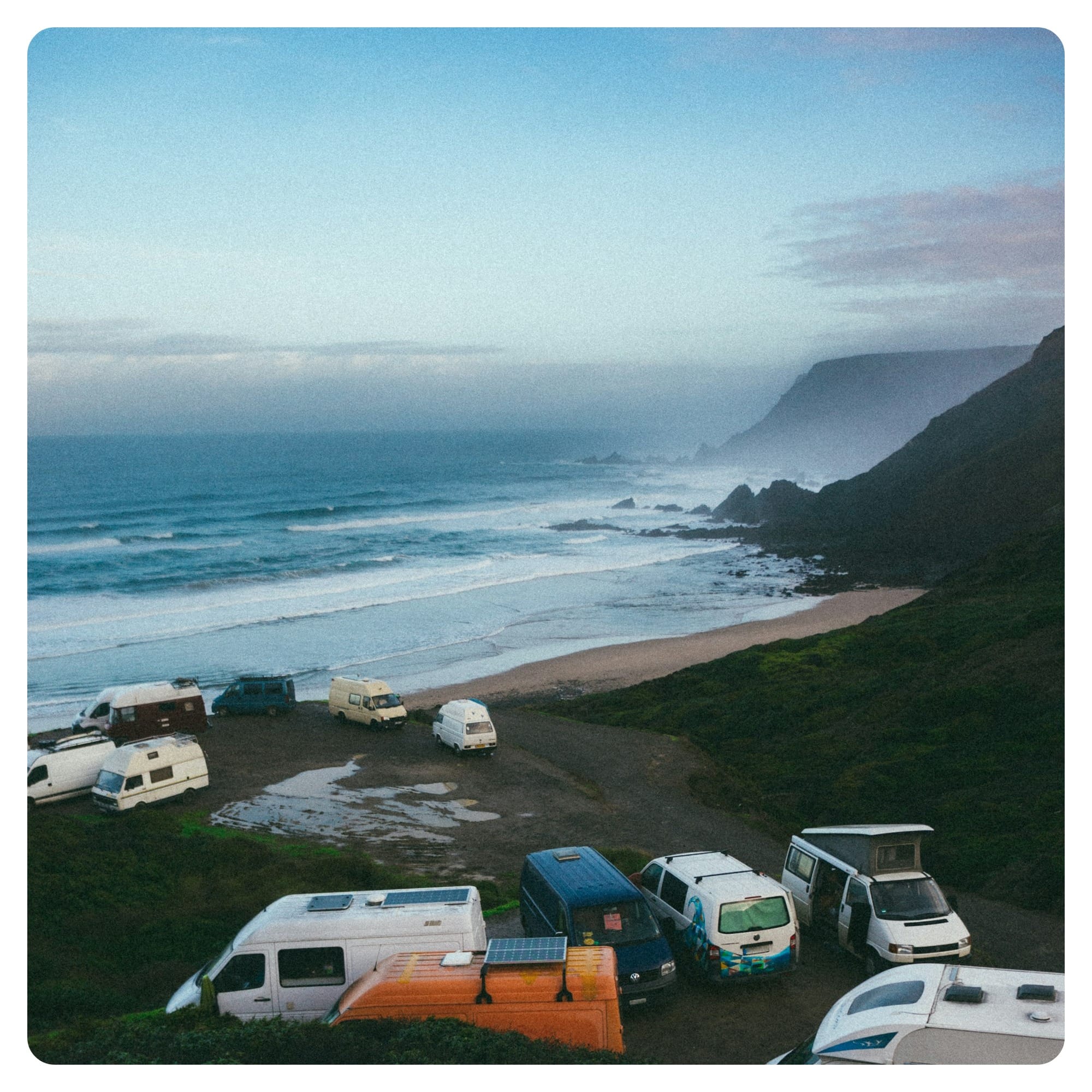 a group of campers parked on a beach next to the ocean