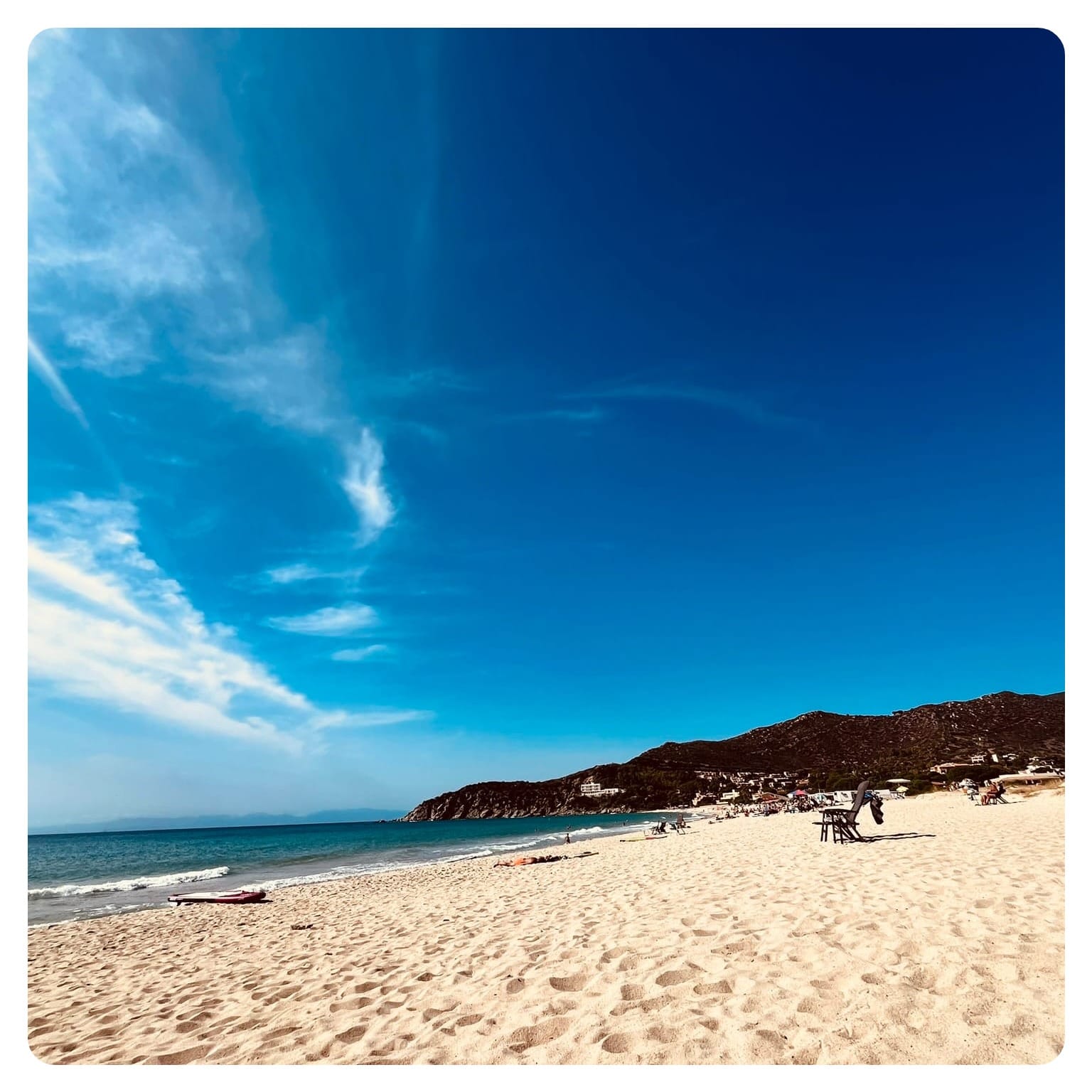 view of sandy beach with blue sky and sunbathers